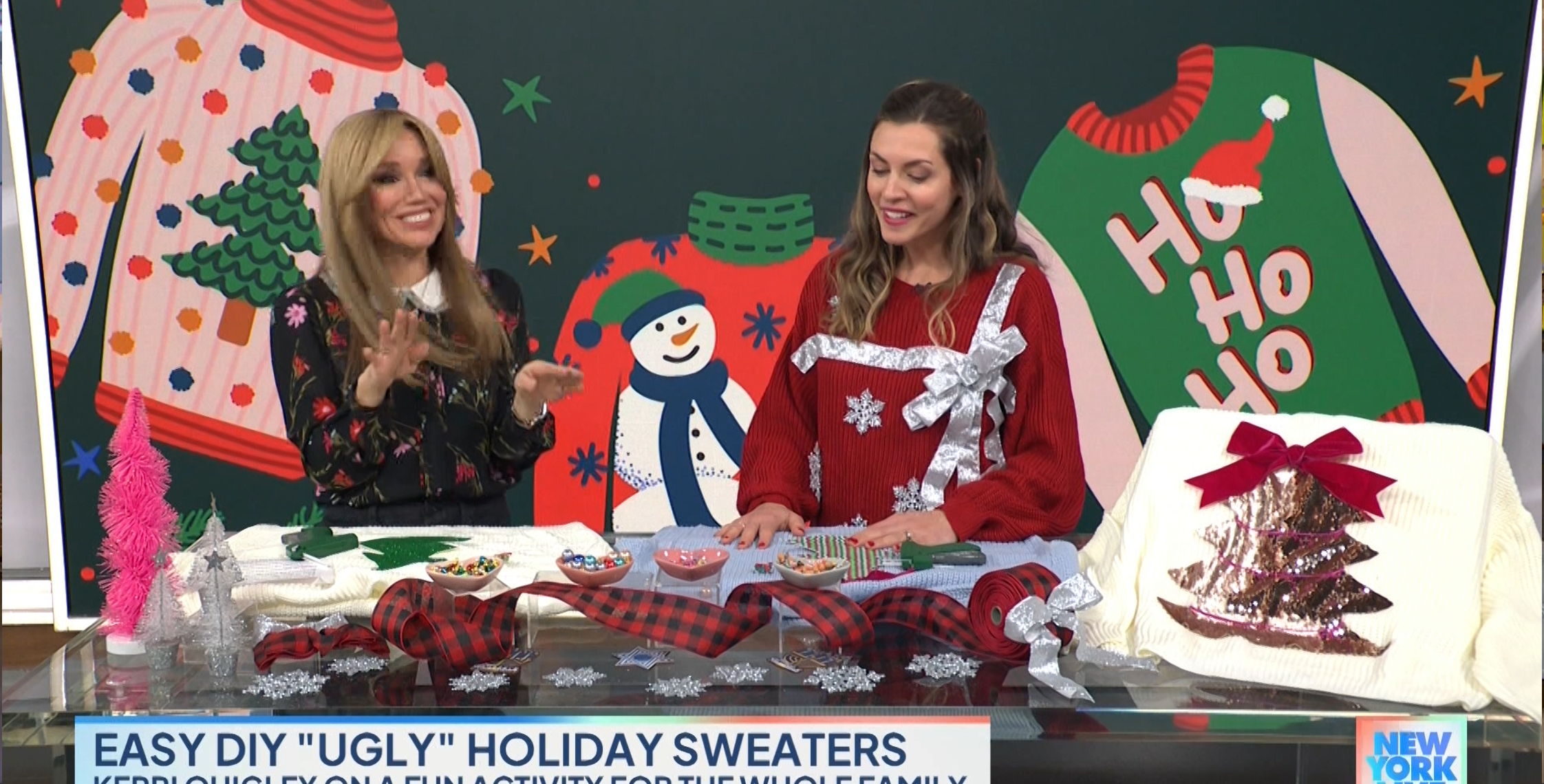 Two women are demonstrating how to make "ugly" holiday sweaters on a TV show set decorated with festive holiday images, including a snowman and holiday sweater cutouts. About them are craft supplies, completed sweater decorations, and a "New York Live" logo.