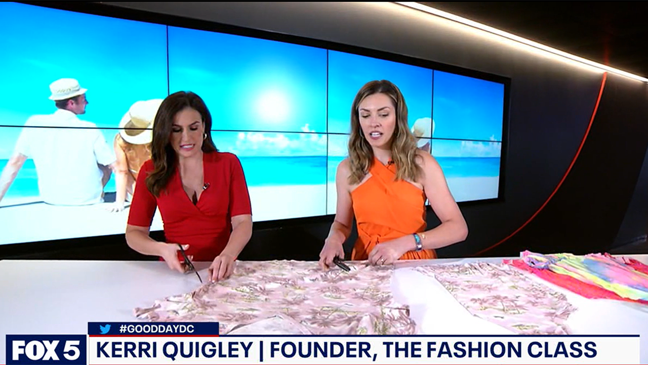 Two women are featured on a TV show set with an ocean scene backdrop. They are cutting fabric on a table. A banner at the bottom reads "FOX 5," "#GOODDAYDC," "Kerri Quigley | Founder, The Fashion Class." About the scene, one woman wears a red dress; the other, an orange dress.