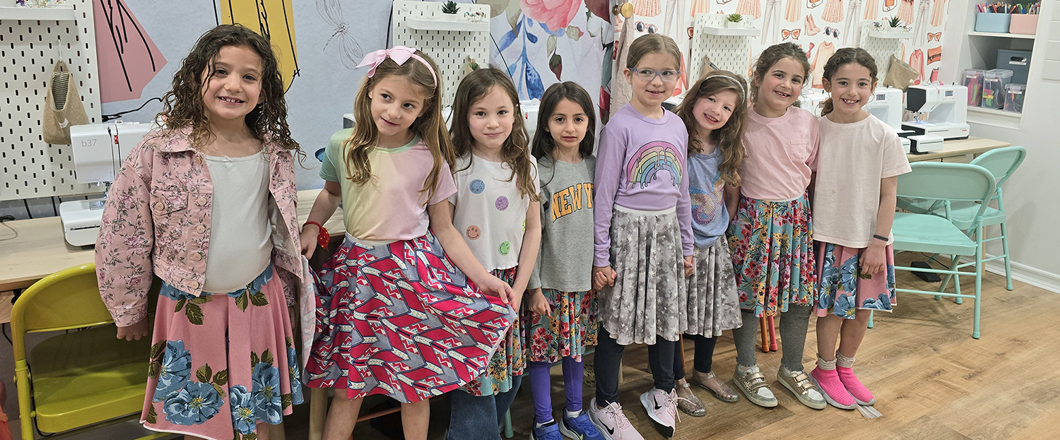 girls standing in front of sewing machines